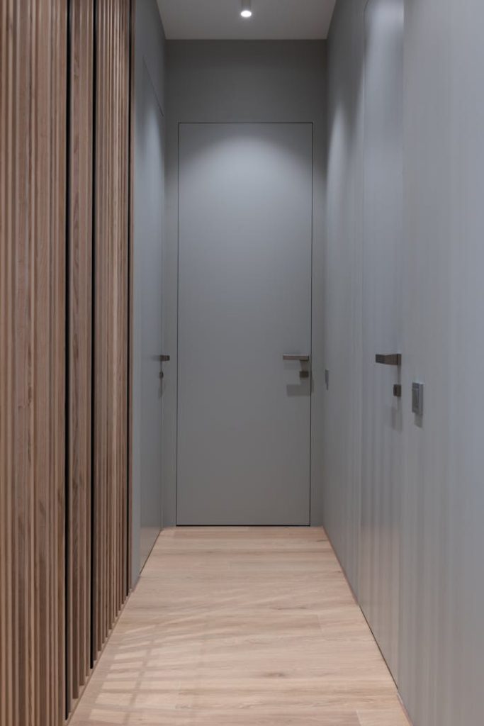 Interior of light empty narrow hall with gray doors under ceiling with lamps in modern house